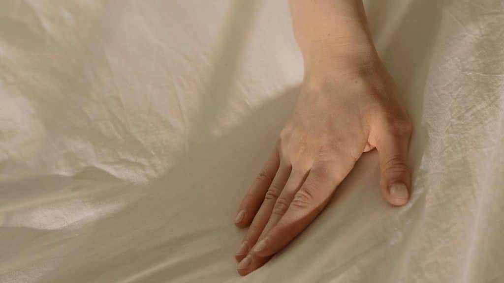 A personโs hand resting gently on a light-colored fabric surface.