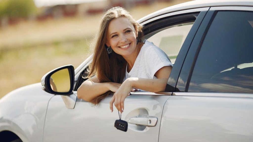 A smiling woman leaning out of a car window holding car keys.