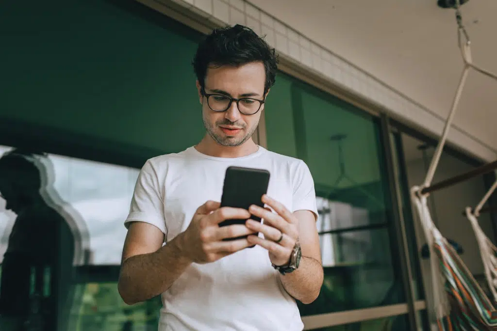 A Young Man Using a Smartphone Standing on a Balcony