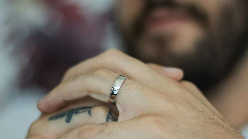 Close-up of a silver wedding band on a man's tattooed finger.