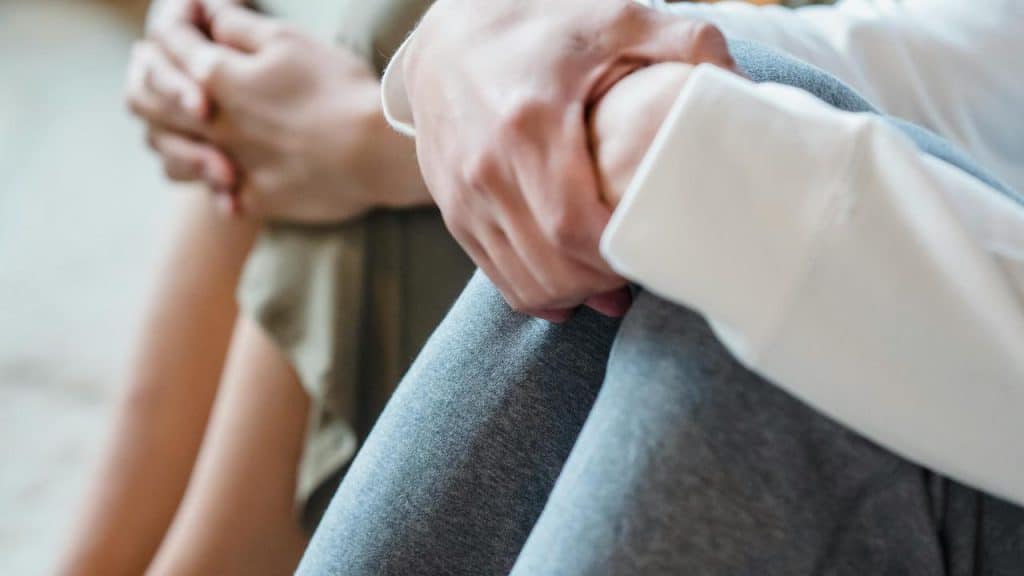A close-up of two people sitting on the floor, one holding their knee with clasped hands.