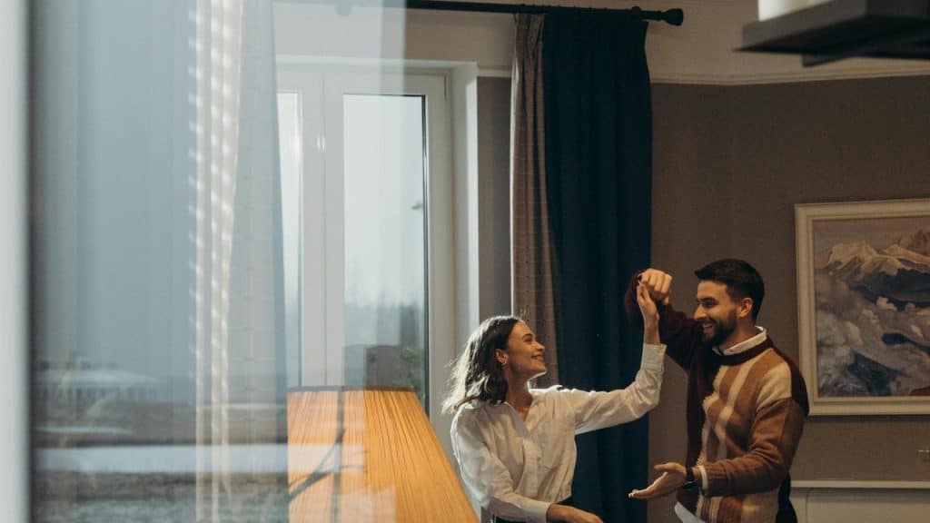A couple dancing together indoors near a large window.