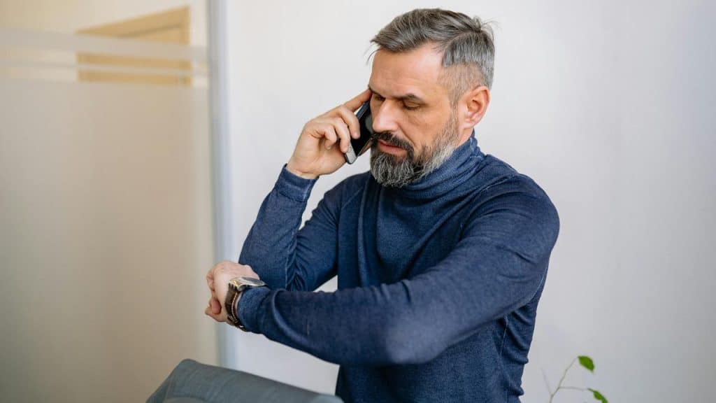 A man man looking at his watch while talking over the phone.