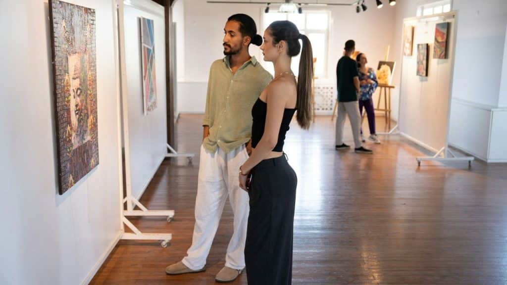 A casually dressed young man and woman are looking at a painting in a bright, spacious art gallery.