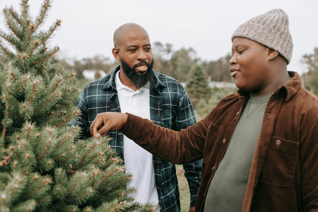 Smiling black dad talking to son touching needles of spruce