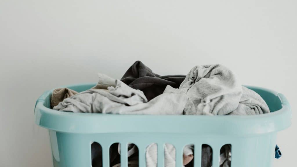 A light blue plastic laundry basket filled with clothes against a plain white wall.