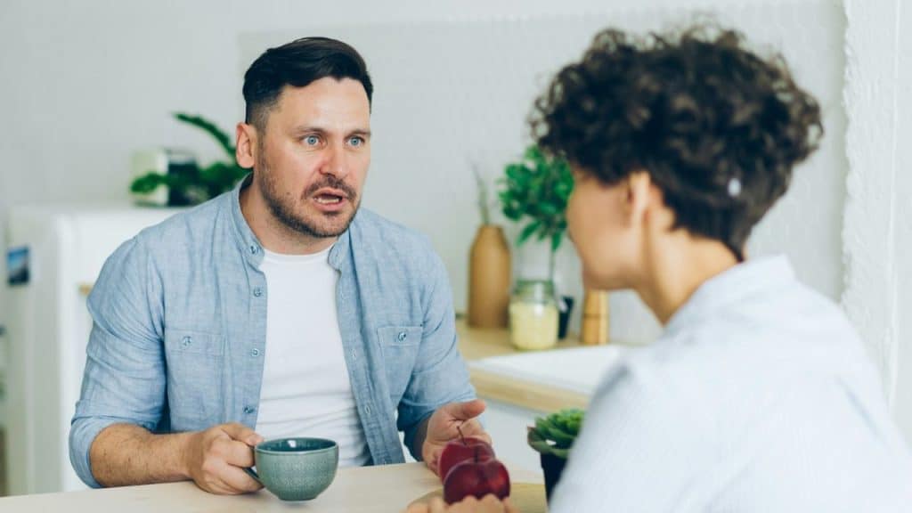 A concerned man with a blue shirt speaks earnestly to a woman across a table.
