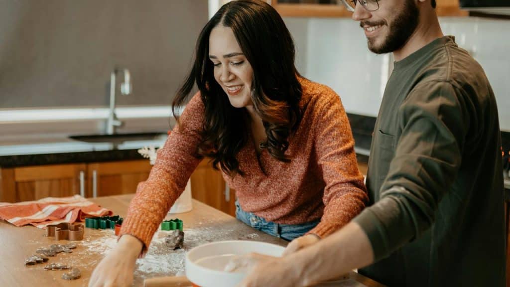 A smiling couple baking together in a kitchen.