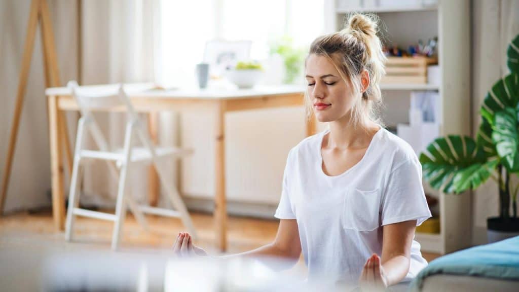 A woman meditating on the floor in a bright room.