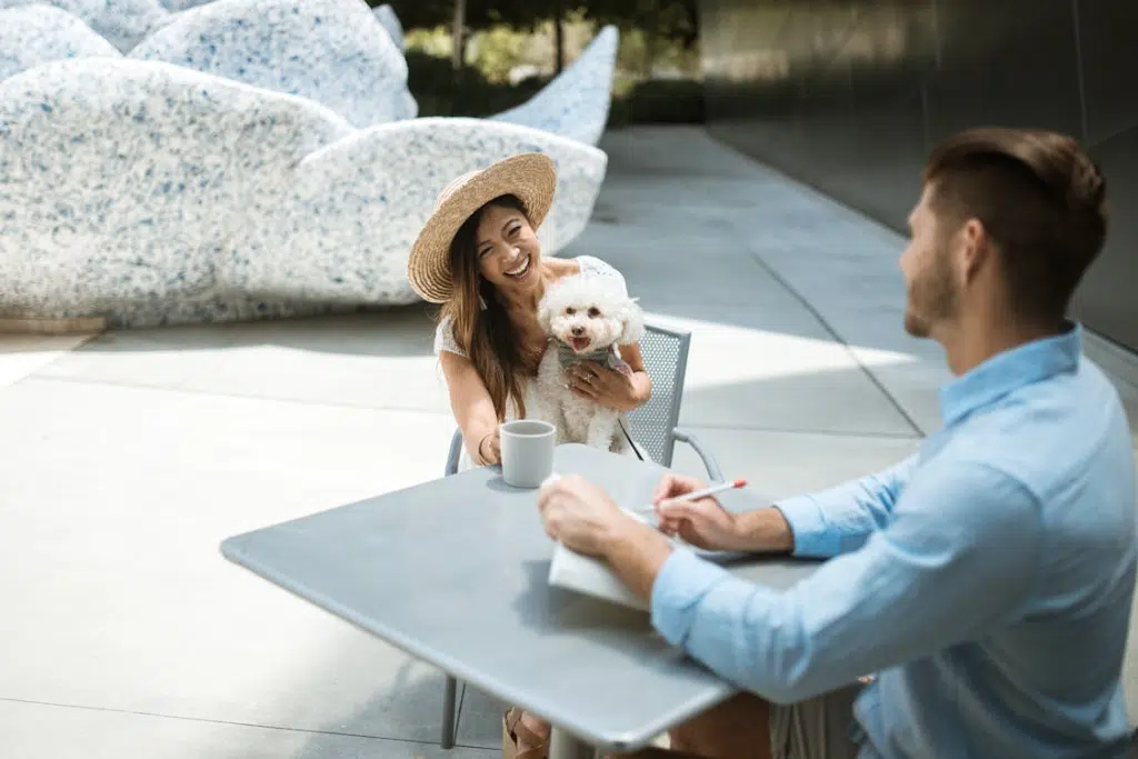 A Woman Holding a Dog while Sitting in front of a Man in Blue Long Sleeves