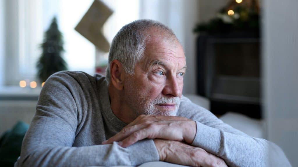 A serious, older man with a white beard and gray hair is leaning on his arms while looking off-camera.