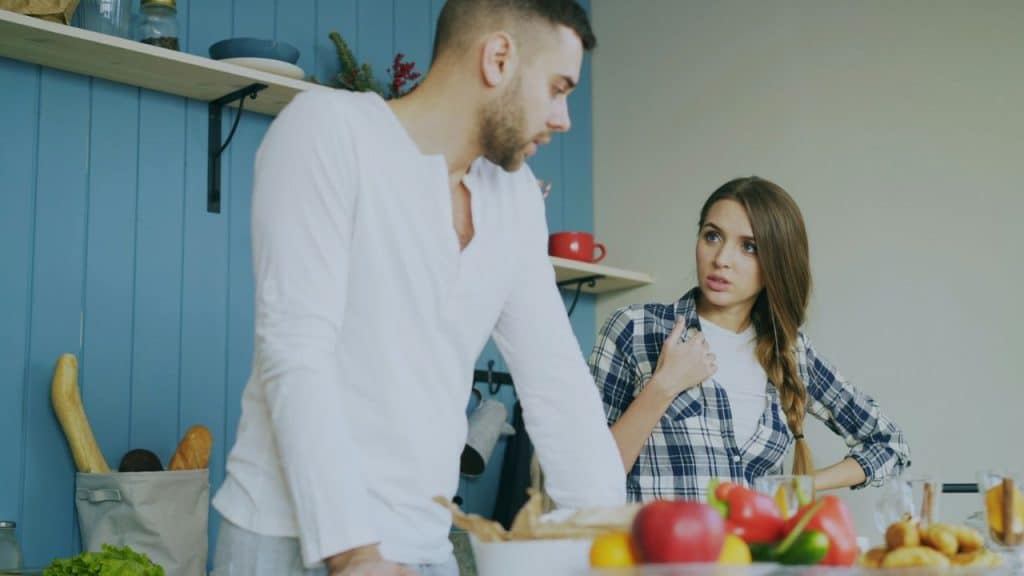 A serious man stands over a woman in a plaid shirt who looks surprised or confrontational.
