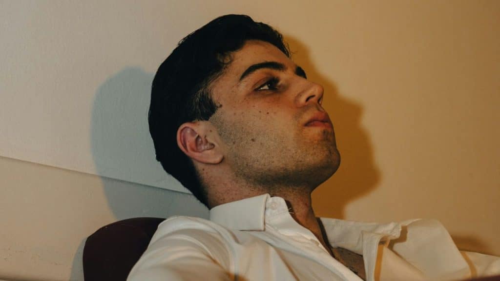 Close-up of a young man with dark hair and a white shirt looking up.