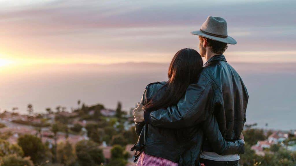 A couple holding each other as they watch the sun set over the ocean.