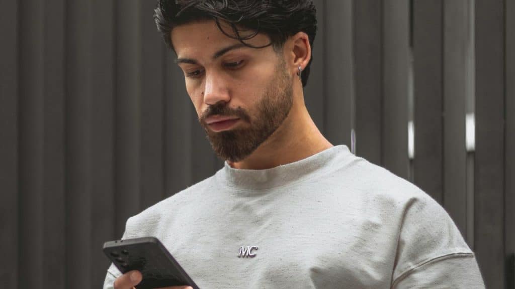 Young bearded man looking intently at a smartphone in his hand.