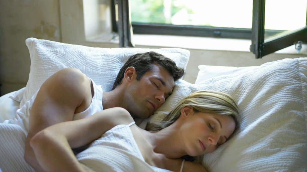 A man and a woman sleeping soundly next to each other in a white bed.