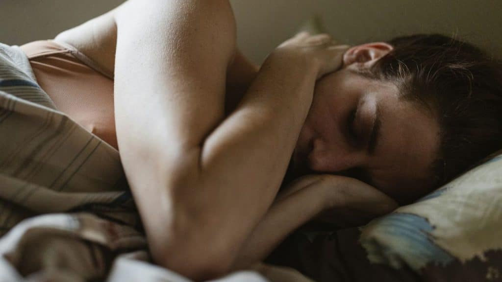 A person is sleeping on their side under covers, with their arms tucked close to their head.