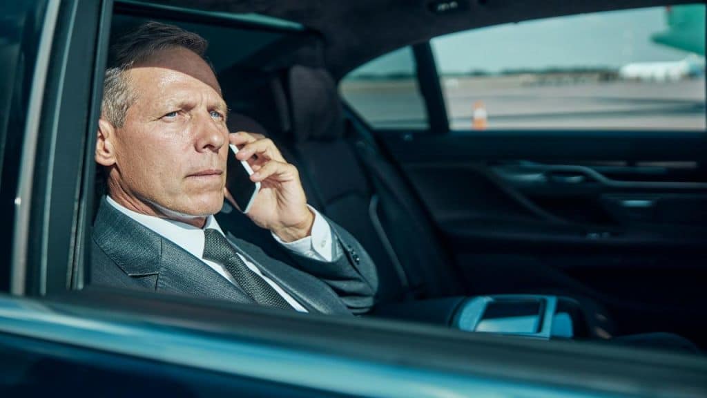A man in a suit talking on the phone while sitting in the backseat of a car.