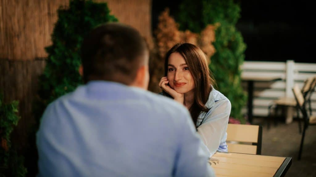 Woman smiling and looking at a man across a table on an outdoor patio at night.