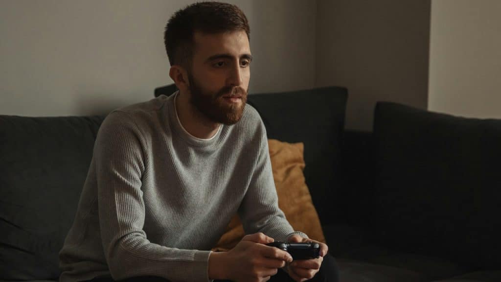 A bearded man sitting on a couch and playing video games. 