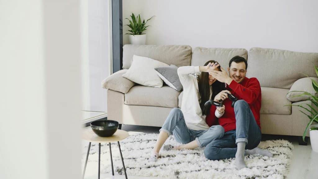 A couple sitting on the floor by a couch laughing while holding game controllers.