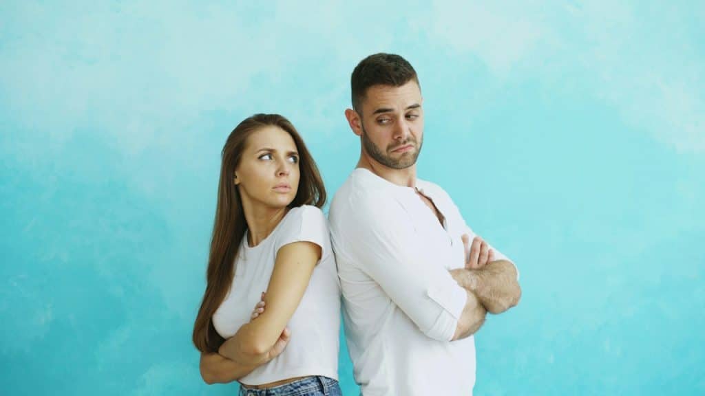 A couple standing back-to-back with arms crossed.