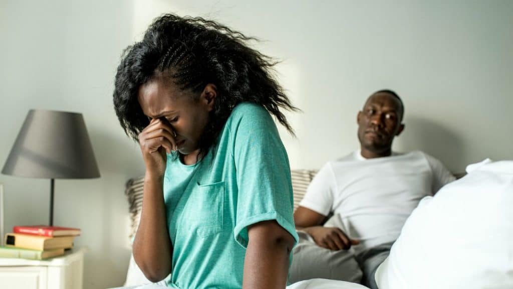 A woman with her head in her hand looks distraught as a man sits behind her.