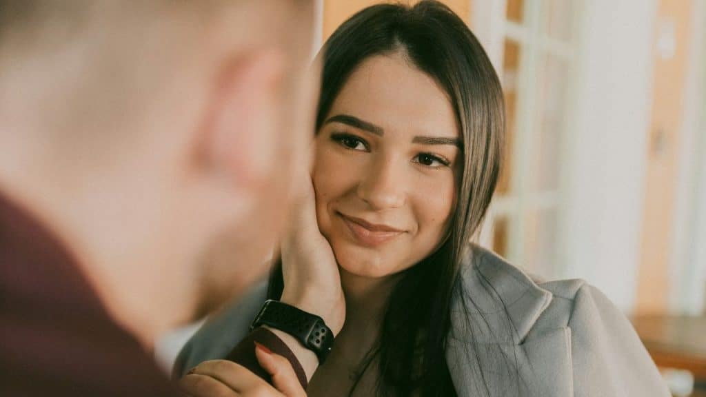 A woman smiles while a man's hand is on her cheek in a warm-toned setting.