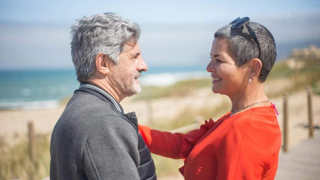 A smiling couple standing close together on a beachside walkway.