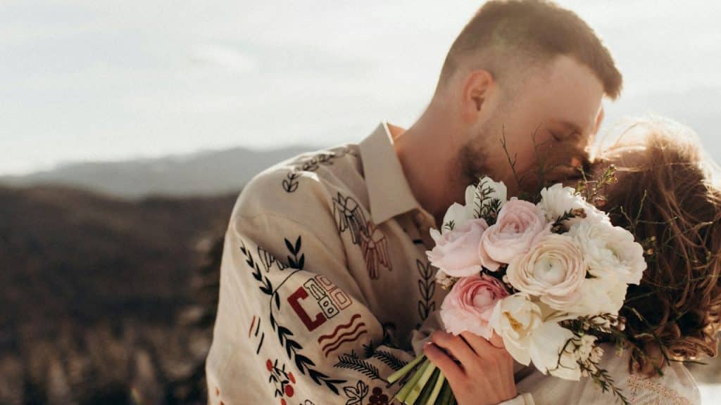 A man kissing a woman holding flowers.