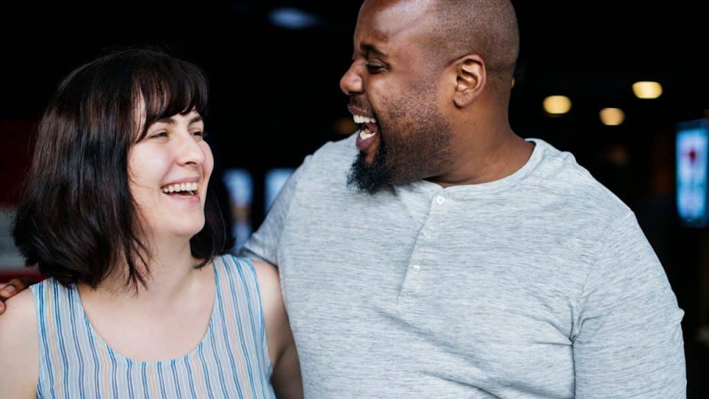A happy couple is laughing together, with the man's arm around the woman.
