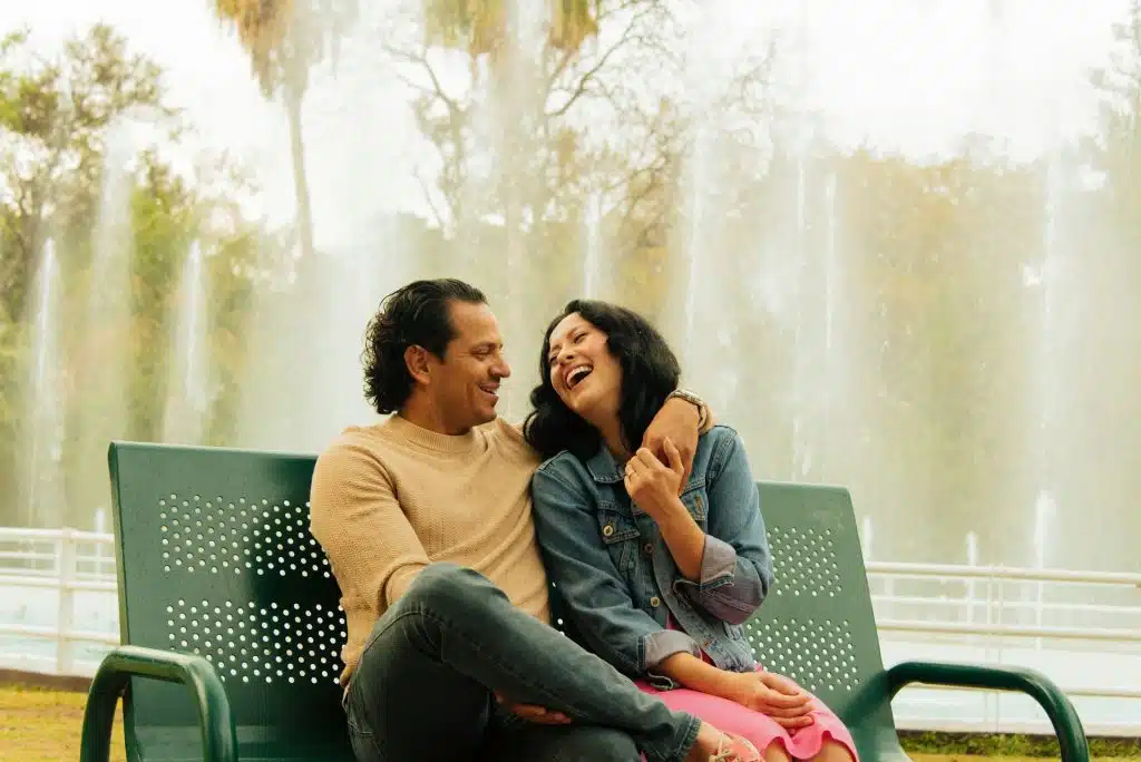 A couple laughing happily while sitting on a bench outdoors.