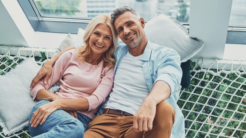 A couple lying on a hammock and smiling up at the camera.