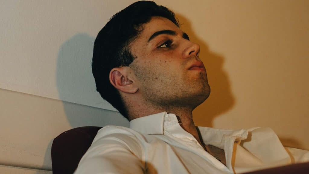 A man in a white collared shirt leans back, looking up and away from the camera.