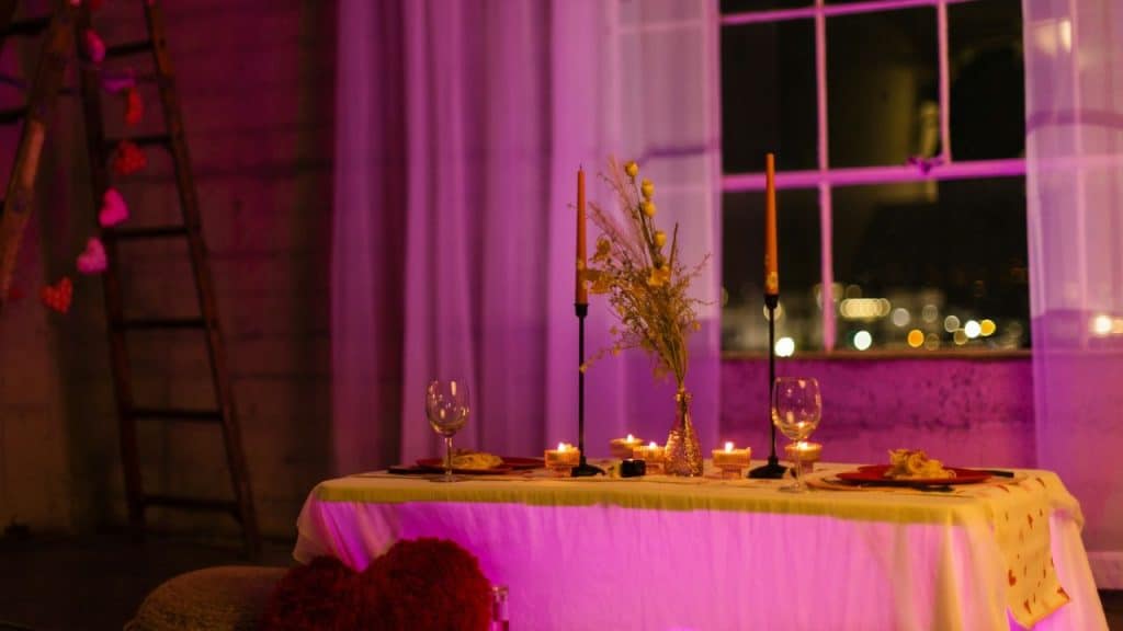 A dinner table set with candles and wine glasses, bathed in pink and purple light.