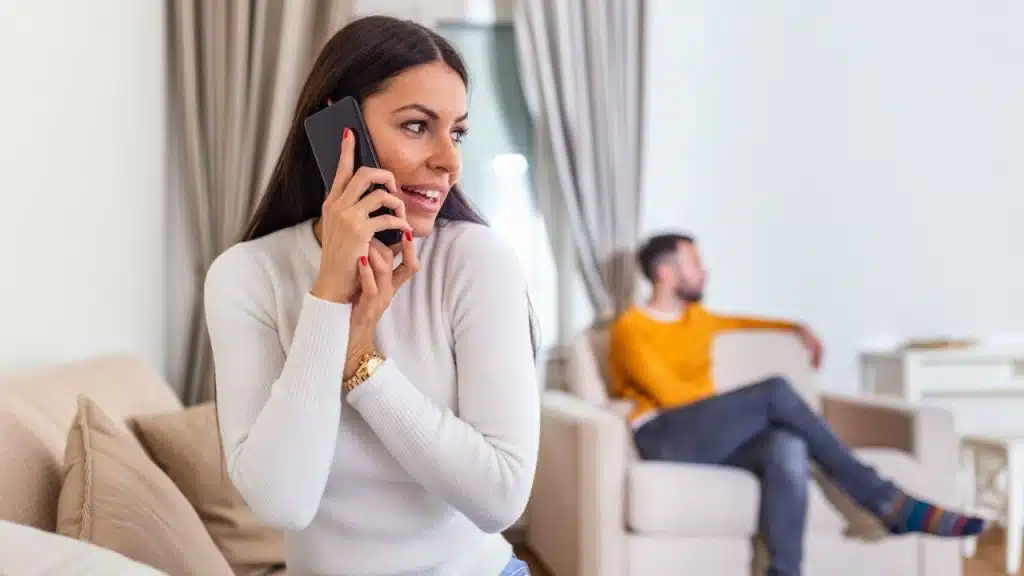 Woman on phone call smiling while a man sits in the background.