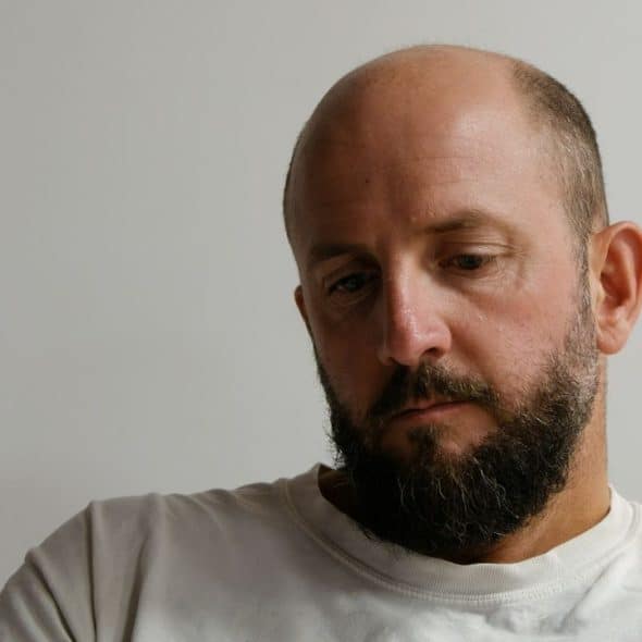 A bald man with a beard and white shirt looks down.