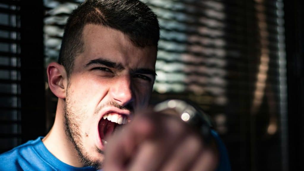 Angry young man yelling and pointing directly toward the camera.