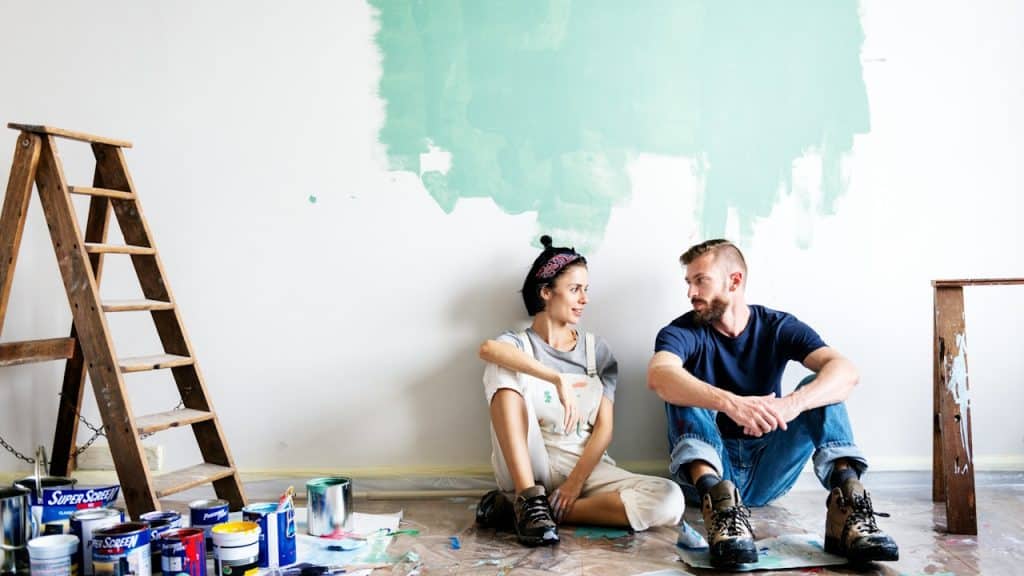 A couple painting a wall and taking a break while sitting on the floor.