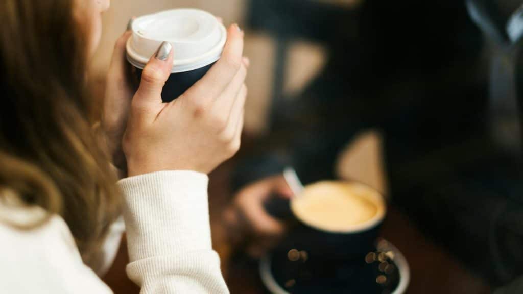 A person holding a takeaway coffee cup while sitting across from someone with another cup.