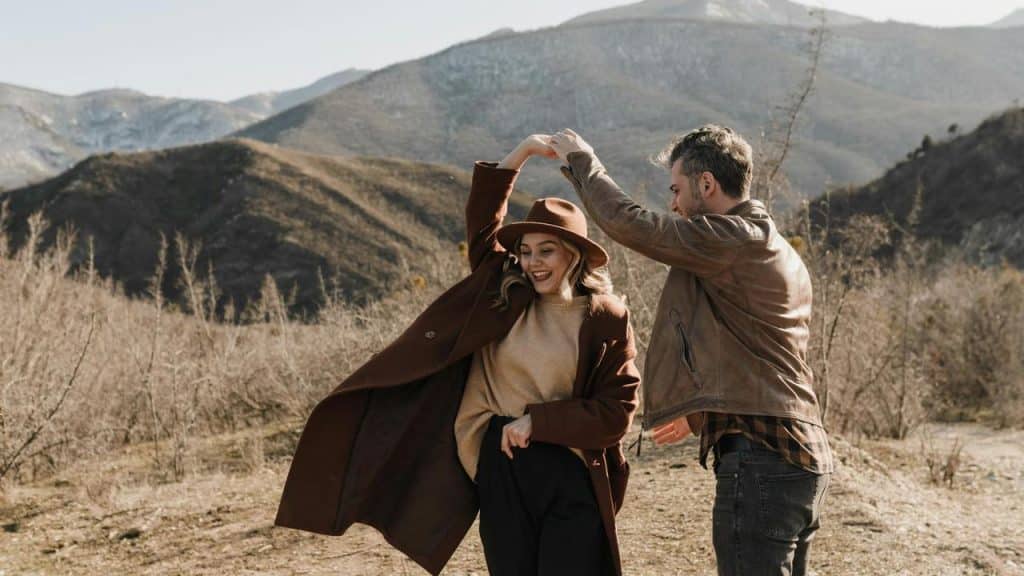A couple dances joyfully outdoors with mountains in the background.