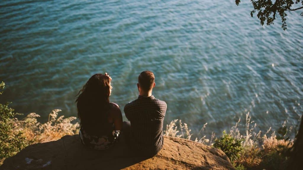 A couple sitting on a rocky cliff overlooking the water.