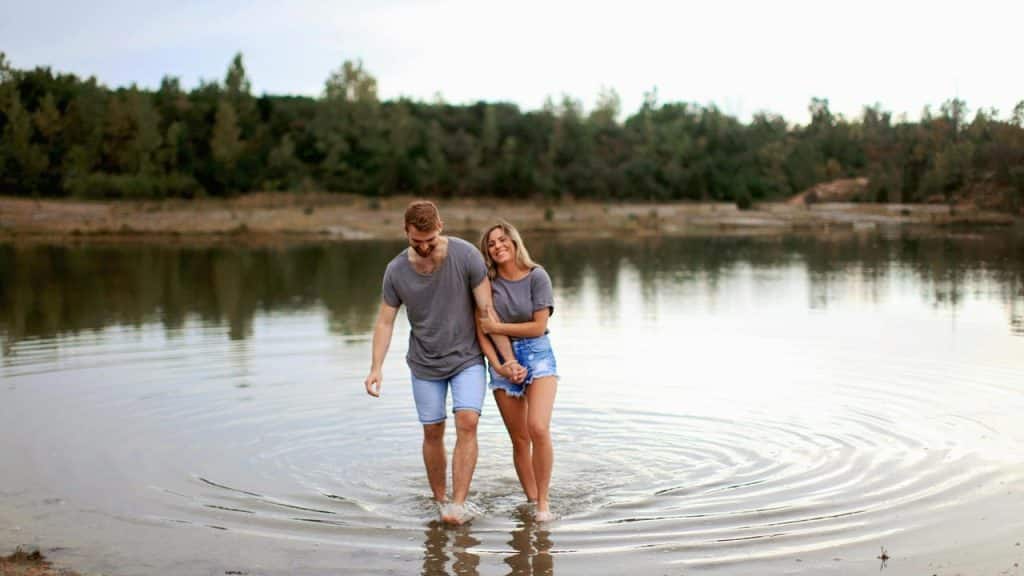 A couple walking hand in hand through shallow water at a lake.