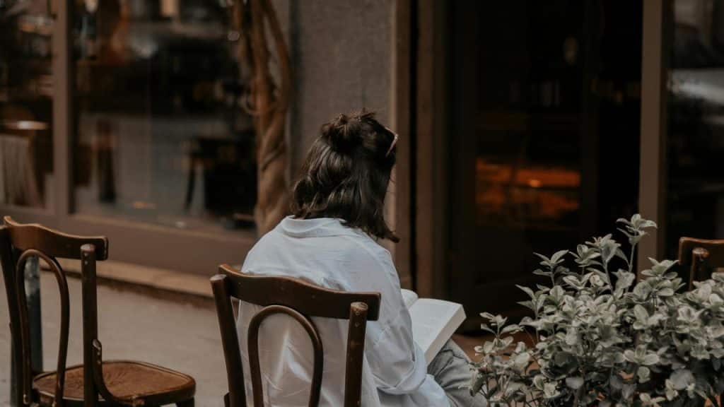 A woman sitting outside a cafรฉ reading a book.
