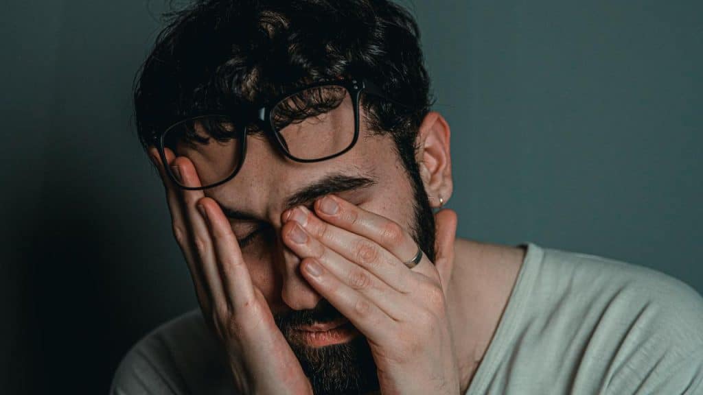 A man wearing glasses resting his face in his hands, appearing tired or stressed.