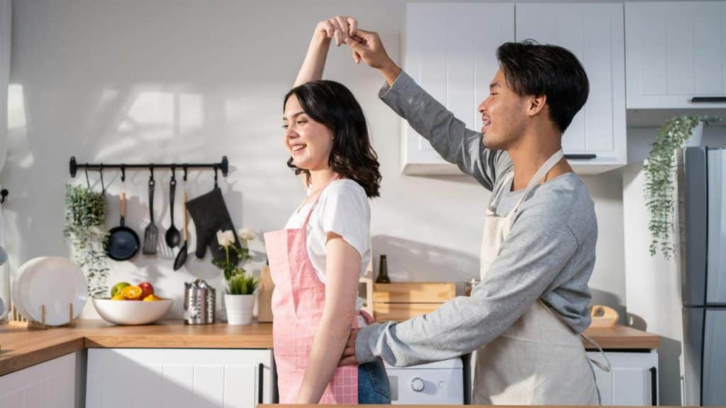 A couple dances playfully together in a bright, modern kitchen.
