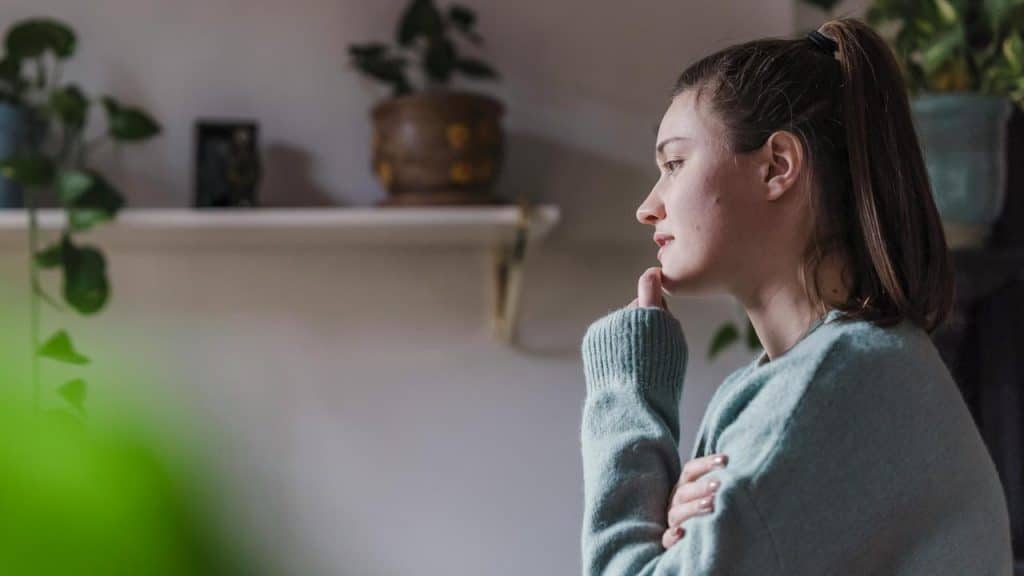 A person sitting indoors, resting their chin on their hand and appearing deep in thought.