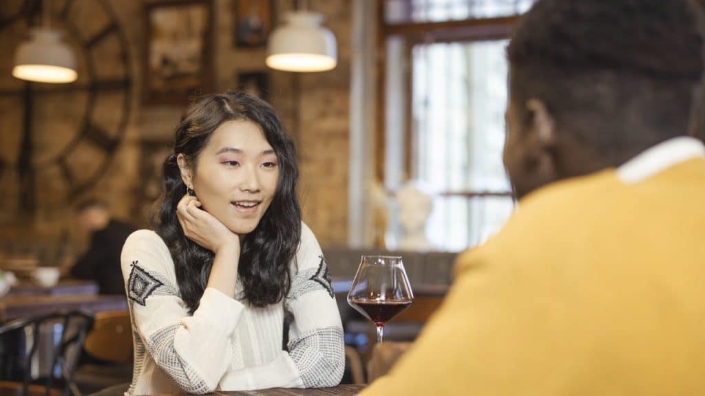 Woman with long, dark hair talking to a man over a glass of red wine in a dimly lit restaurant