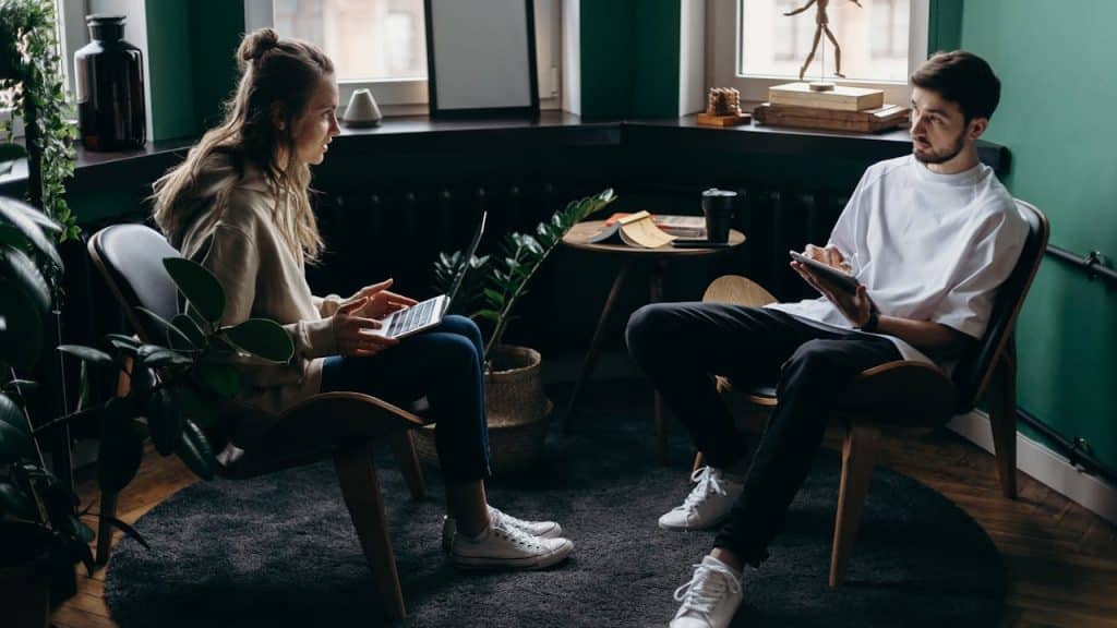 A man and a woman working on laptops while sitting on chairs.