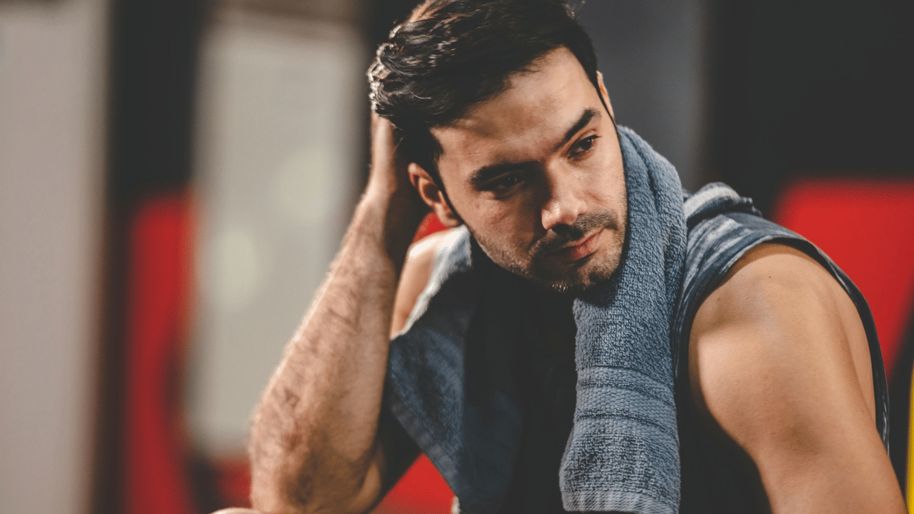 A man with a towel draped around his neck is resting after a workout.